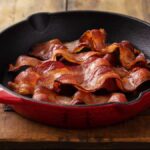 Bacon is crispier if 1 common ingredient is added to the pan before cooking